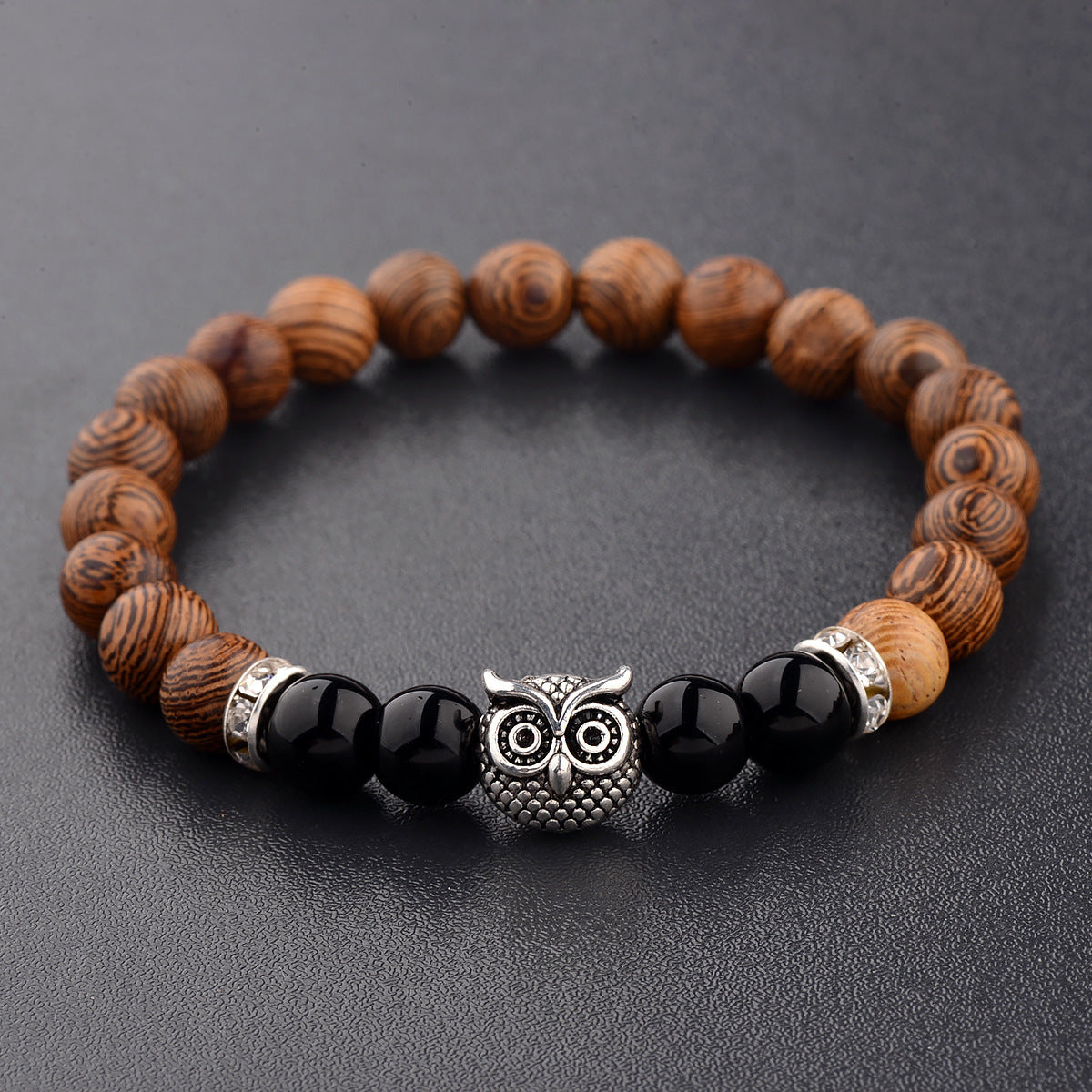 Close-up of owl-engraved frosted stone beads on wood grain bracelet.