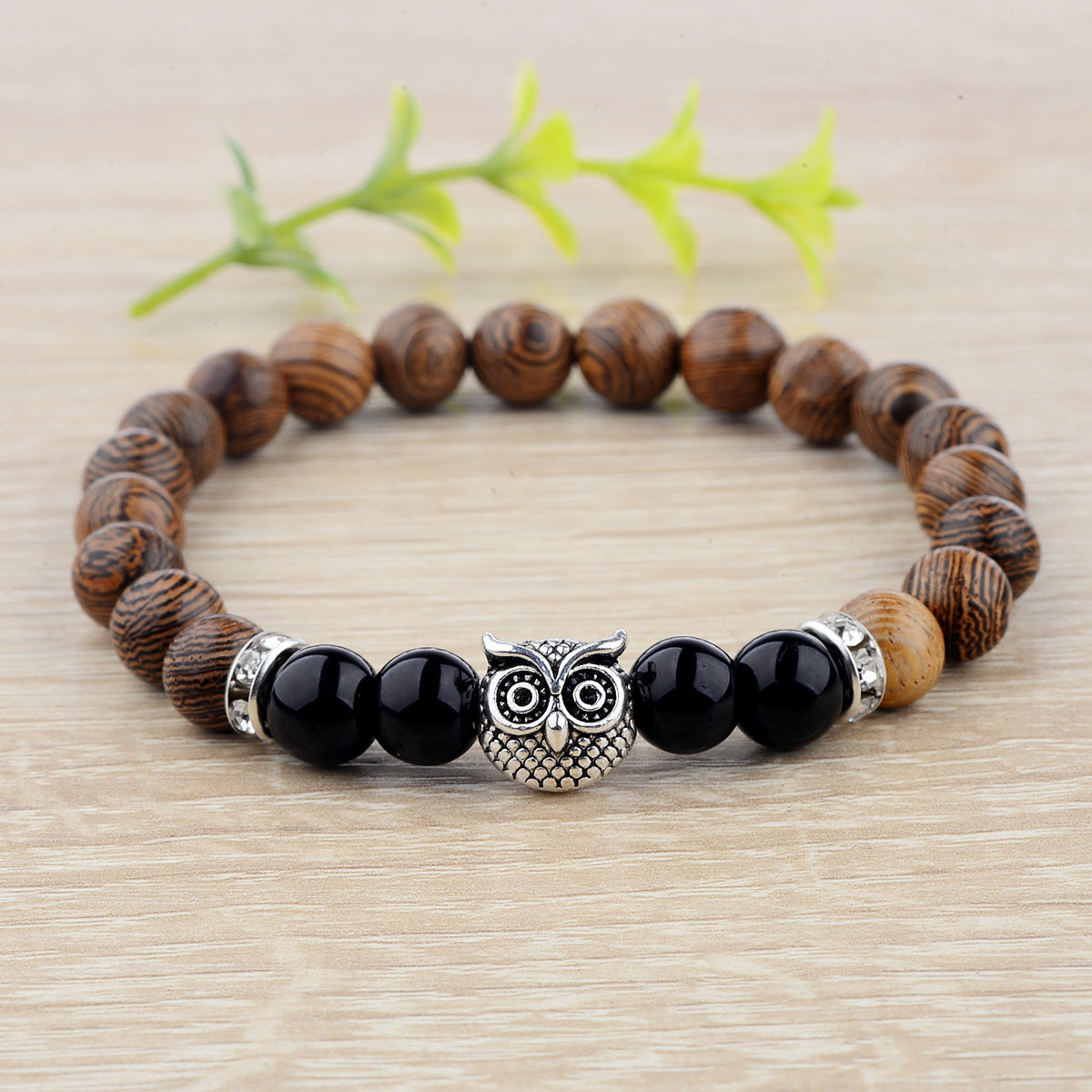 Close-up of owl-engraved frosted stone beads on wood grain bracelet.