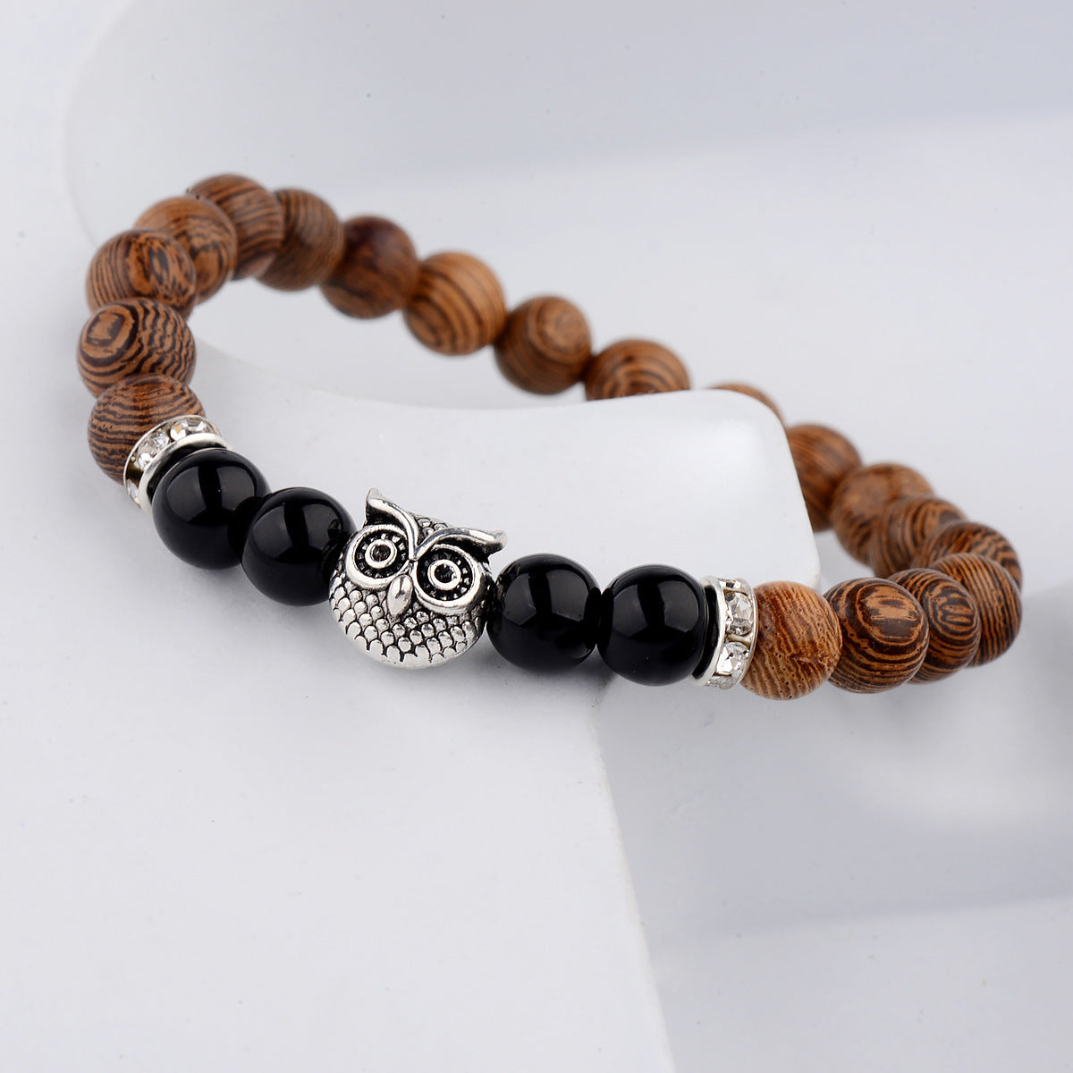 Close-up of owl-engraved frosted stone beads on wood grain bracelet.