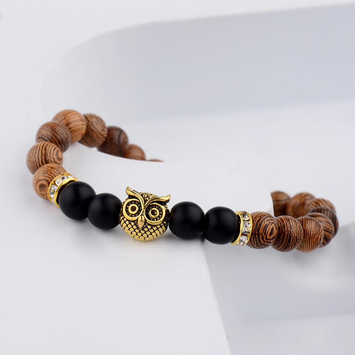 Close-up of owl-engraved frosted stone beads on wood grain bracelet.