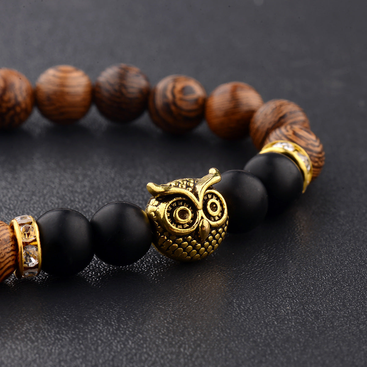 Close-up of owl-engraved frosted stone beads on wood grain bracelet.